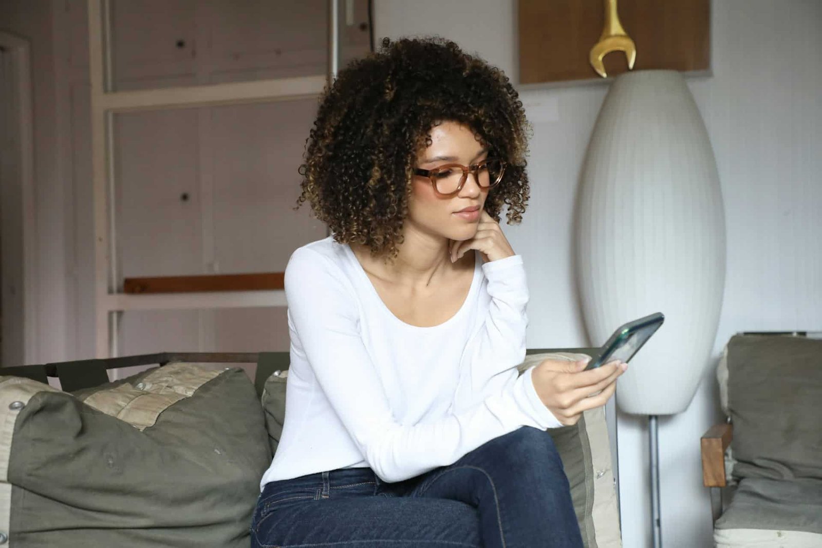 Woman-looking-down-her-phone-while-seated-on-bed Woman looking down her phone while seated on bed