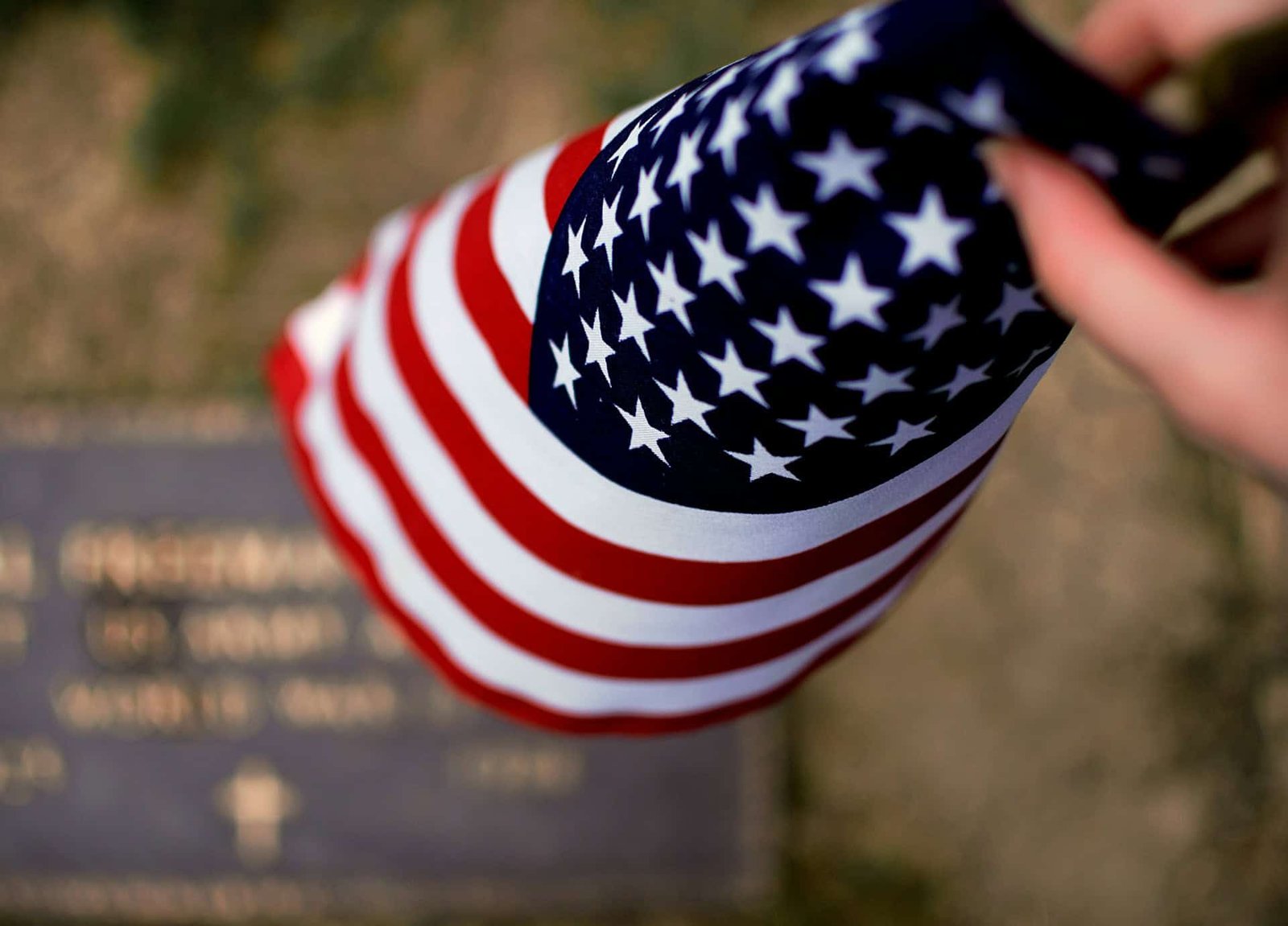 person-folding-small-american-flag-with-gravestone-in-background Person folding a small American Flag with a gravestone in the background